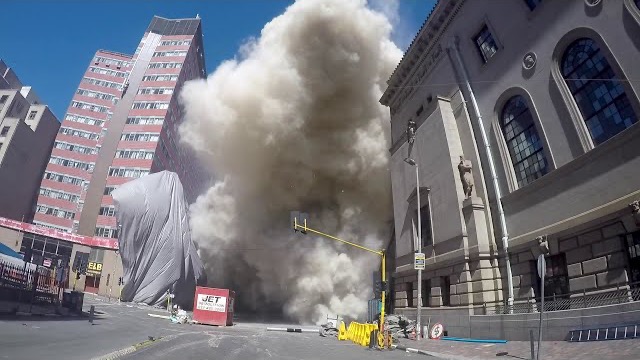 Frame from the film: dust rising between buildings at street level as the tower comes down