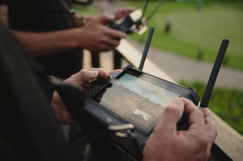 Close-up of a DJI controller showing the live camera feed, with the second operator’s controller behind it